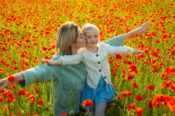 Happy spring family. Carefree mom with a child girl in a field of red poppies enjoys nature. Mother and little daughter in the poppy field. A young woman with her daughter in in a poppy field. — Stockfoto