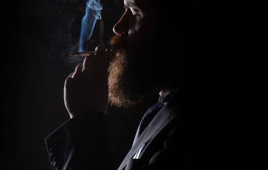 Siyah arka planda sigara içen genç adamın yüzünde koyu bir gölge var. Sigara içen adam.