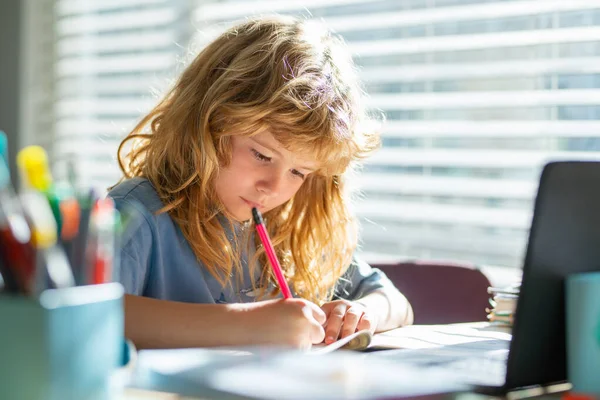 Schrijven van kinderen op school. Schooljongen maakt notities in het copybook tijdens online les op laptop thuis. Leuke jongen die huiswerk maakt. Kinderonderwijs. — Stockfoto