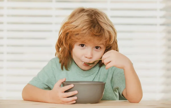 Portret van een schattig kind dat soep eet of ontbijt bij de tafel thuis met lepel. Kinderen gezond voedsel. — Stockfoto