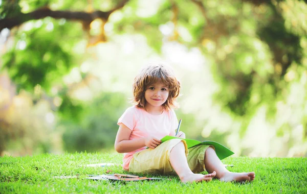 Χαριτωμένο μικρό μαθητή σπουδάζει στο πάρκο και χαμογελώντας Εξωτερική εκπαίδευση των παιδιών. — Φωτογραφία Αρχείου