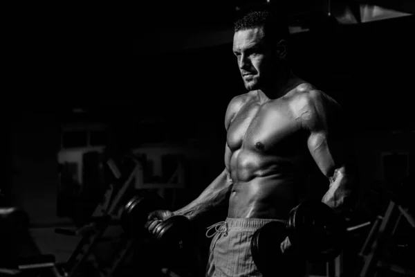 Un uomo forte con i manubri in palestra. Bodybuilder bicipiti di formazione da esercizi di allenamento. Sportivo con corpo atletico. — Foto Stock