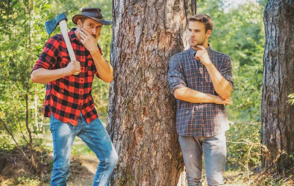 Woodcutters lumberjacks. Hipsters men on serious face with axe. Lumberjack brutal and bearded holds axe. Two lumberjacks in forest. Man in hat looks brutally. — Fotografia de Stock