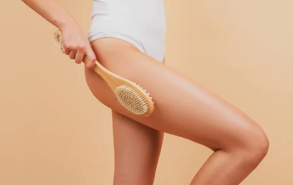 Woman legs with clean skin. Female buttocks ass without cellulite. Skin treatment. Cosmetology, spa cosmetic products, beauty close-up. Woman makes massage with a wooden soft massage brush for body. — Photo