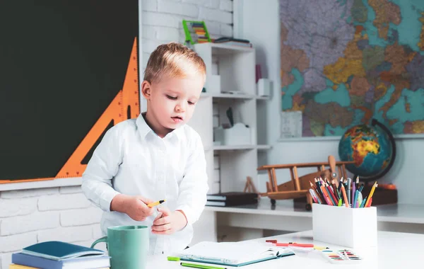 Los niños se preparan para la escuela. Interiores de la escuela.Feliz niño trabajador lindo está sentado en un escritorio en el interior. — Foto de Stock