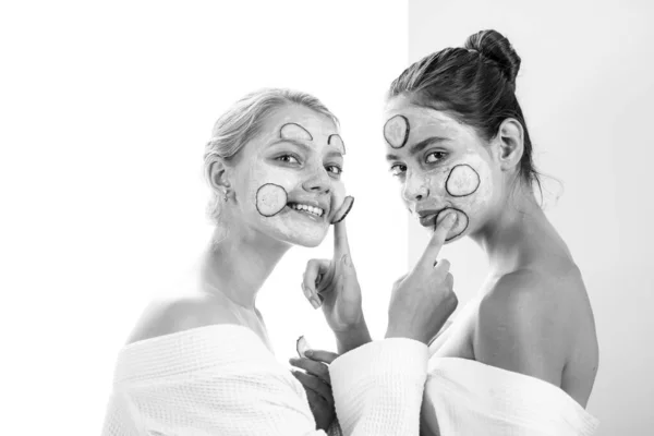 Happy smiling friend girls with mask at no makeup face having fun and making healthy natural skincare procedures. Two girls with clay mask and cucumber slices at face. — Foto de Stock