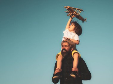 Baba ve oğul. Oyuncak uçaklı çocuk babasının omuzlarında oturuyor. Mutlu baba çocuk anı. Baba, oğlunu gökyüzünde oyuncak uçakla oynarken sırtında taşıyor..