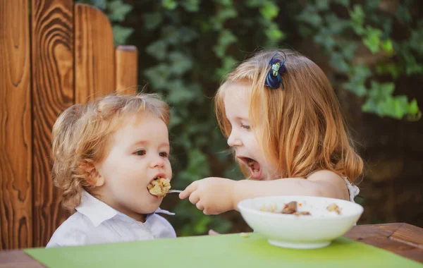 Küçük komik kız kardeş bebeği besliyor. Tatlı komik bebeklerin yemesi, bebek maması, sağlıklı çocukların kahvaltısı. Afiyet olsun. — Stok fotoğraf