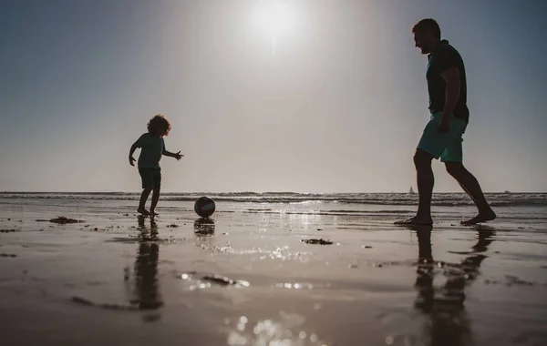 父と息子はビーチでサッカーやサッカーをします。夏の日に子供の男の子とパパ. — ストック写真