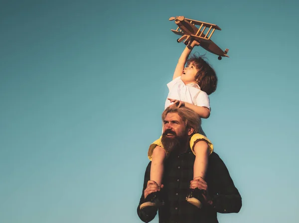 Ojciec i syn. Chłopiec z zabawkowym samolotem siedzącym na ramionach ojców. Szczęśliwy ojcowski moment. Ojciec podpiera swojego chłopca na niebie, podczas gdy on bawi się zabawkowym samolotem. — Zdjęcie stockowe