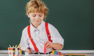 Resim ödevi yapan, elinde kalem tutan, yazı yazan okul çocuğu. Çocuk ilkokulda resim çiziyor. Çocuk sanatı, yaratıcılık çocukları.