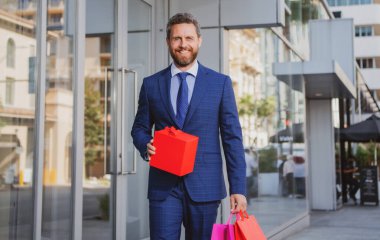 Alışveriş torbaları taşıyan, şehirde yürüyen bir iş adamı..