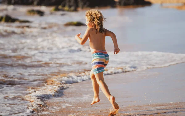 Niño corriendo a través del agua cerca de la orilla a lo largo de la playa. Un niño corre a lo largo de la costa. Resto de niños en vacaciones de verano. — Foto de Stock