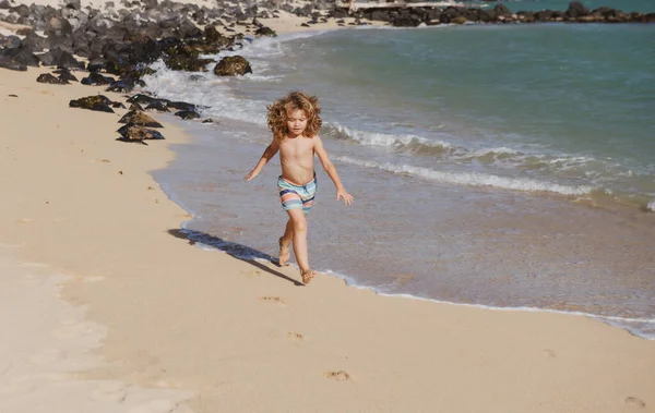 Happy kid boy haben Spaß am tropischen Meer Strand. Lustiges Kinderrennen mit Spritzern am Wasserbecken entlang der Surfkante. Kinderaktivitäten in den Sommerferien. — Stockfoto