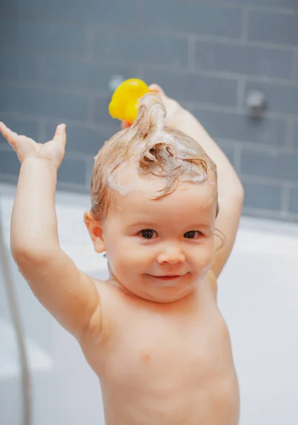 Uśmiechnięty dzieciak w łazience z zabawkową kaczką. Kąpiel. Szczęśliwy dzieciak z pianką mydlaną na głowie. — Zdjęcie stockowe
