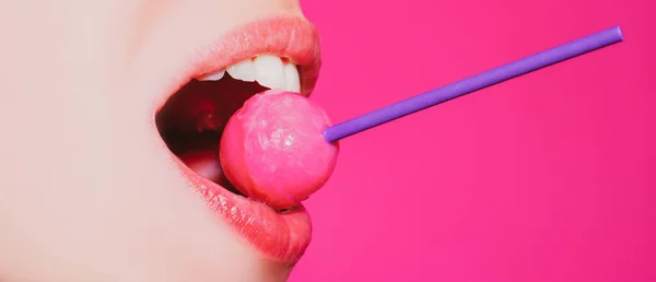 Snoep likken. Lollipop model. Vrouwelijke lippen zuigen een snoepje. Glamor sensueel model met rode lippen eet zweet lolly pop geïsoleerd op roze. — Stockfoto