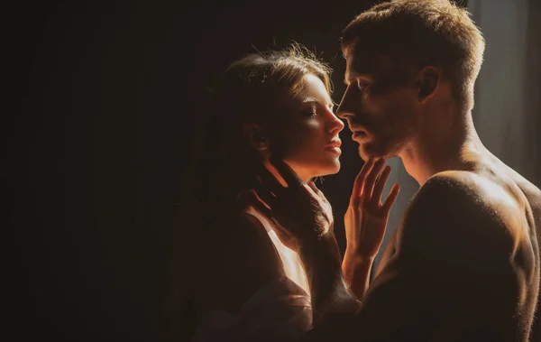 Romantic couple in love looking at each other, embracing and kissing on black background. Beautiful loving couple posing on dark backgroung with night lights. — Fotografia de Stock