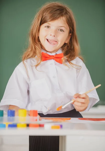 Ritratto di divertente ragazza lingua sorridente felicemente mentre godendo arte e artigianato lezione di disegno. Ragazza a scuola disegna con vernici. Bambini artista creatività. Divertenti emozioni per bambini. — Foto Stock