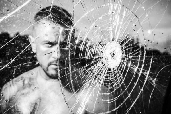 砕いたガラスの後ろにマゾ男のガラスくず。セクシーなヒスパニック系の男が鏡を壊した。ガラスの弾丸の穴ヒットしたせいでガラスが割れた怒りだ破壊だテストだ盗難だ感情的な放電ガラスの彫刻家. — ストック写真
