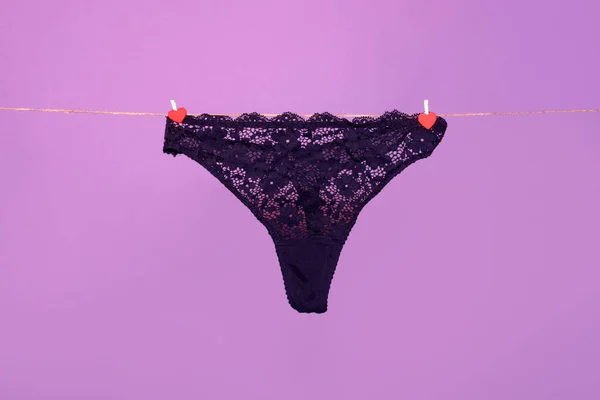 Panties. Female lace lingerie. Womans erotic black underwear panties. Womens panties hanging on rope isolated on purple background. — Zdjęcie stockowe
