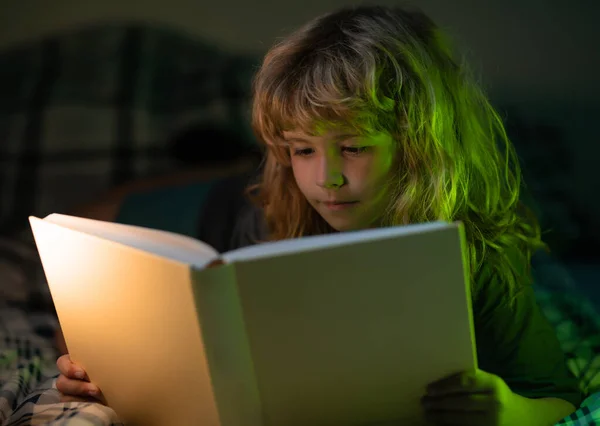 Child read fairy tale from book. Child little boy reading a book in the dark home. Kids face with night light. — Stok fotoğraf