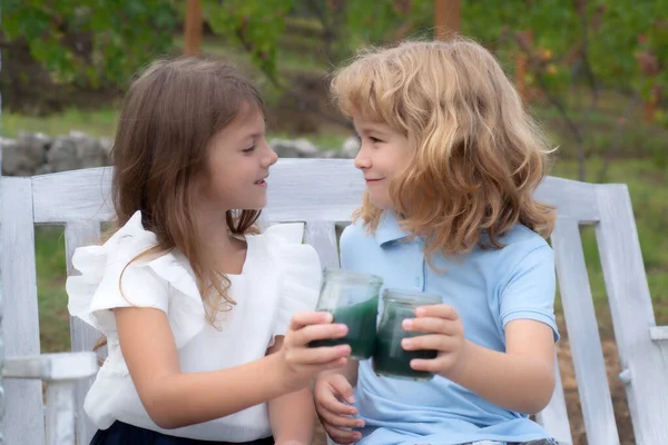 Two children drink smoothie, kids summer cocktail outdoors. Portrait of adorable brother and sister smile and laugh together while sitting on swing outdoors. Happy lifestyle kids. — Stockfoto