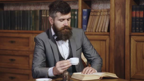 Men reading a book on bookshelf background. Literature library. Reader sits in interior and reads book. Bearded man in classic suit with cup of english tea. Mature man enjoys reading. — Stockvideo