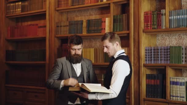 Business employees chatting in library. Concentrated professor and student. Man in classic suit read book in library. Classic literature. Man reading book in bookshelf in a library. — Vídeos de Stock
