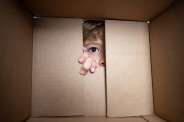Heyecanlı çocuk kutuya bakıyor, karton kutu taşıyor. Gözlerini kapat ve bak. Paketleme veya açma kavramı.