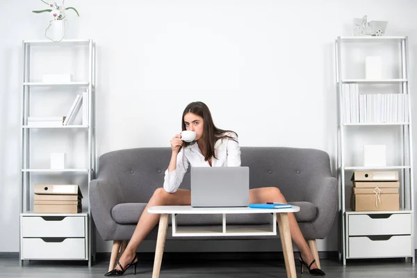 Sexy businesswoman with sexy legs. Seductive woman drinking coffee, sensual secretary sit on sofa in office. Seductive girls at work. — Stockfoto