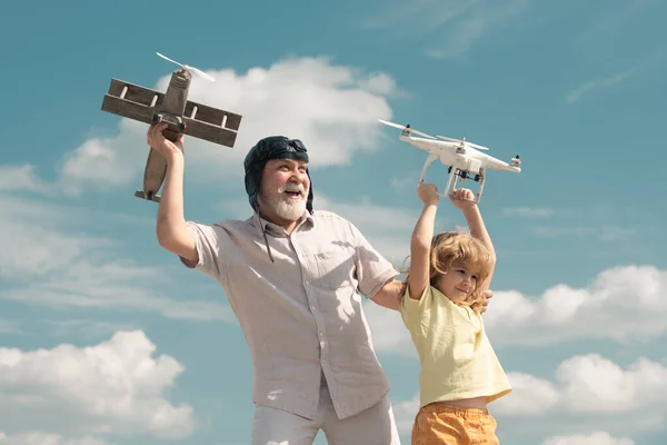 Junger Enkel und alter Großvater halten Flugzeug und Drohnen-Quad-Copter gegen den Himmel. Kinderflieger mit Flugzeug träumt vom Fliegen. Familienbeziehung Großvater und Kind. — Stockfoto