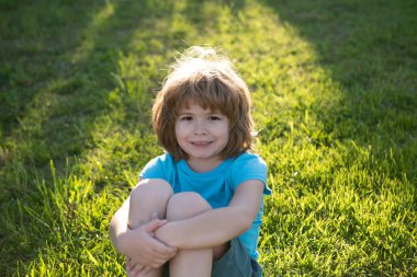Yakından küçük şirin bir çocuk portresi. Dışarıdaki çimlerin üzerinde mutlu çocuk portresi. Duygusal küçük çocuk, şaşırmış küçük çocuklar. Çocuklarla yaz tatili. Sarışın çocuk, duygusal yüz..