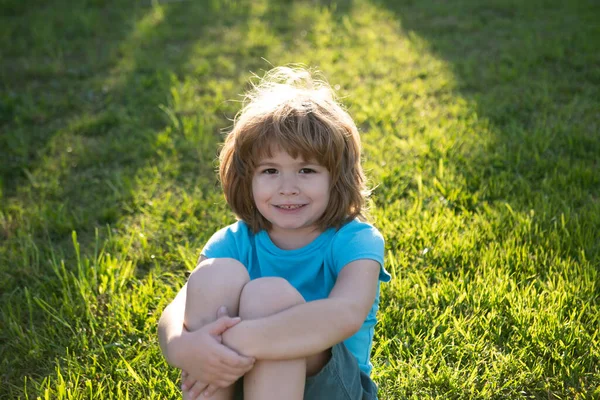 Yakından küçük şirin bir çocuk portresi. Dışarıdaki çimlerin üzerinde mutlu çocuk portresi. Duygusal küçük çocuk, şaşırmış küçük çocuklar. Çocuklarla yaz tatili. Sarışın çocuk, duygusal yüz..