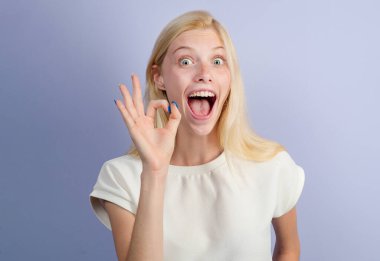 İzole edilmiş arka plandaki kadın parmaklarıyla tamam işareti gösteriyor. Komik genç kız iyi bir jest yapıyor. Gülümseyen neşeli, genç ve güzel bir kız. Stüdyonun arka planında. Kadın duyguları.