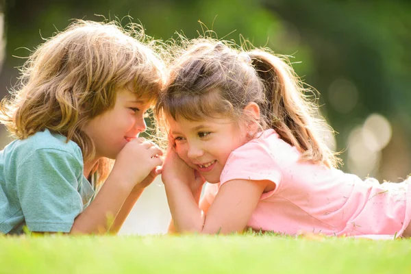 Маленький хлопчик і дівчинка кращі друзі обіймаються. Діти цілуються один з одним з любов'ю в літньому парку. Маленькі друзі. Блондинка діти брат і сестра лежать на траві . — стокове фото