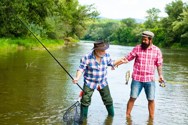 Due uomini amici pescatori pesca sul fiume. Vecchio padre e figlio con canna da pesca a riva del fiume. Attività ricreative. Felice uomo eccitato amici. — Foto Stock