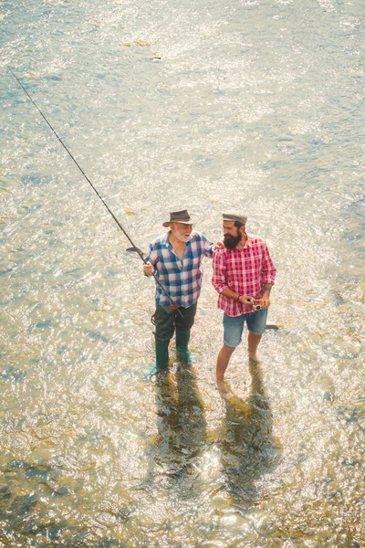 Due uomini amici pescatori pesca sul fiume. Vecchio padre e figlio con canna da pesca a riva del fiume. Attività ricreative. — Foto Stock