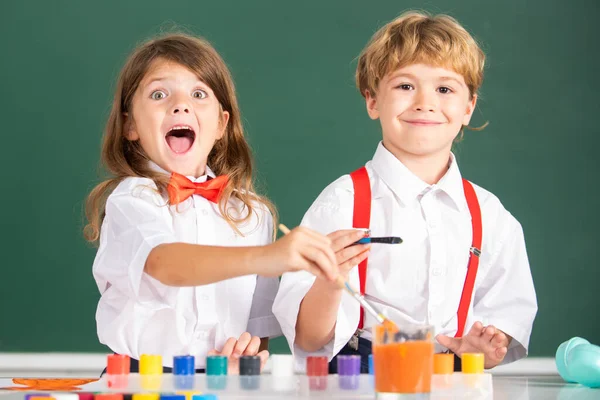 Roliga glada barn flicka och pojke ritning med färgläggning pennor. Söta skolbarn målar i skolan, tittar på kameran. Måleri lektion, teckning konst. — Stockfoto