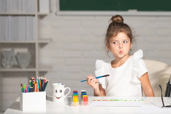 Criança menina desenha em sala de aula sentado em uma mesa, se divertindo no fundo do quadro-negro da escola. Aprendizagem infantil, habilidades de artesanato infantil. — Fotografia de Stock
