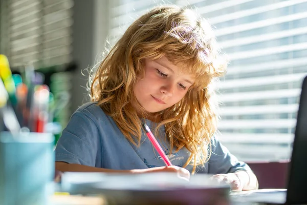 Портрет школяра сидить на столі, роблячи домашнє завдання. Концентрована серйозна дитина, що пише в блокноті. Фокусований школяр вивчає та готується до іспитів . — стокове фото