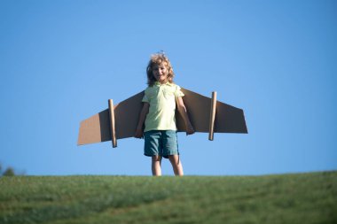 Çocuk parkta karton oyuncak kanatlarla oynuyor. Çocuk günü kavramı. Pilot kostümlü çocuk oynuyor ve havacı uzay adamı olmanın hayalini kuruyor. Çocuk özgürlüğü kavramı.
