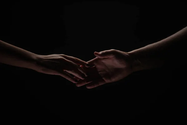 Duas mãos a aproximar-se. Ajudando mão estendida para a salvação em fundo preto isolado. Close-up de homem e mulher mão toque com os dedos. — Fotografia de Stock