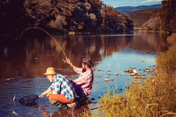 Ritratto di allegro pescatore anziano pesca. Nonno e figlio pescatori. Giovane uomo e un vecchio pesca per filate sul fiume o lago. — Foto Stock