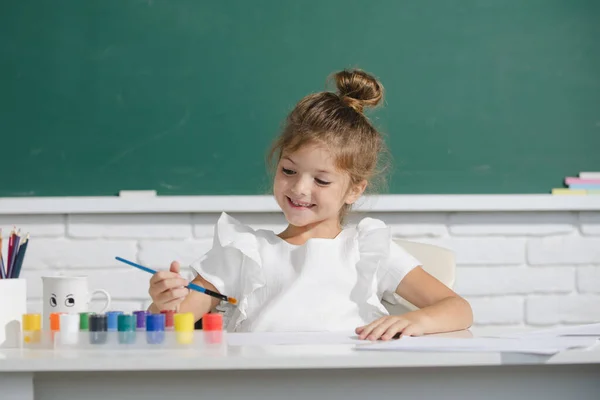 A kislány az iskolában festékkel rajzol. A gyerekek művészi kreativitás. Aranyos iskolás lány rajz az iskolában. — Stock Fotó