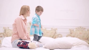 Mutlu tasasız aile evde eğleniyor. Gülümseyen anne ve küçük çocuk rahat yatak odasında rahat bir yatakta birlikte hafta sonunun tadını çıkarıyorlar. Anne ve çocuk yatak odasında konuşuyor..