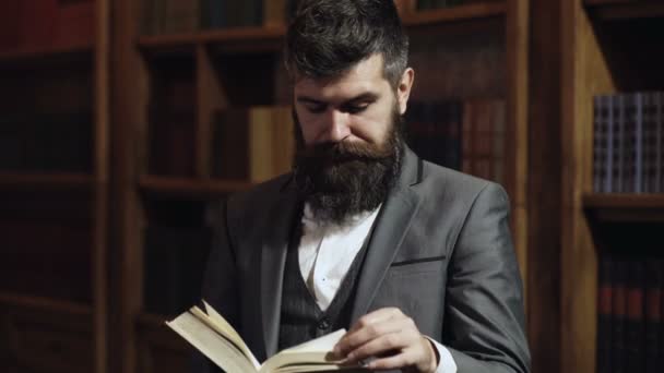 Des hommes lisant un livre sur fond de bibliothèque. Bibliothèque de littérature. Reader est assis à l'intérieur et lit le livre. Homme barbu en costume classique aime lire. — Video
