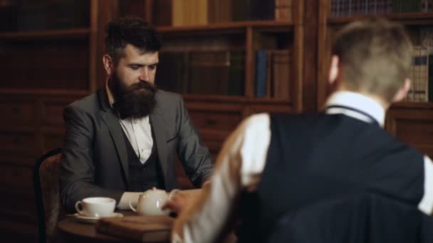 Incontro d'affari. Due uomini che leggono il libro in mano sullo sfondo della libreria. Un bell'uomo ben vestito che discute di ascoltare e parlare. Una conversazione tra uomini. Diritto e giustizia concetto. — Video Stock