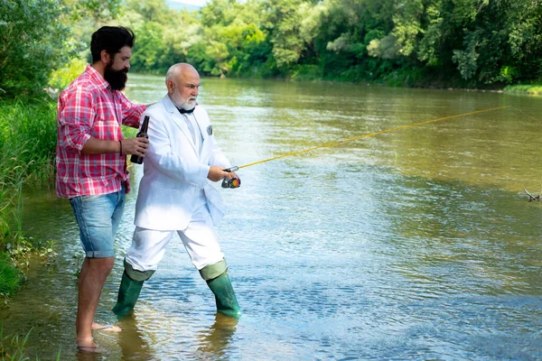 Due uomini amici pescatori pesca sul fiume. Vecchio padre e figlio con canna da pesca a riva del fiume. Attività ricreative. — Foto Stock