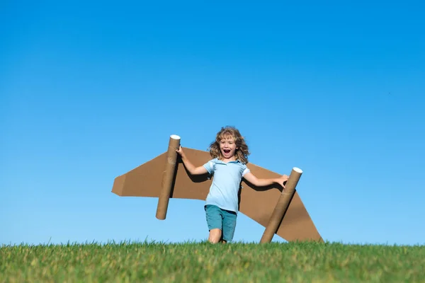 小さな子供は宇宙飛行士やパイロットを演じる。青空を背景に子供。紙の翼ジェットパックの夢を持つ子供たち。子供たちは飛ぶ夢を想像する。おもちゃのジェットパックと面白い子供. — ストック写真