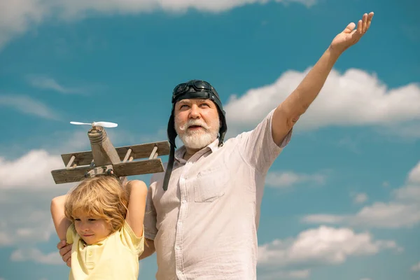 Dziadek i wnuk z samolotem nad błękitnym niebem i chmurami tła. Mężczyźni pokolenie dziadek i wnuk bawią się na świeżym powietrzu. — Zdjęcie stockowe